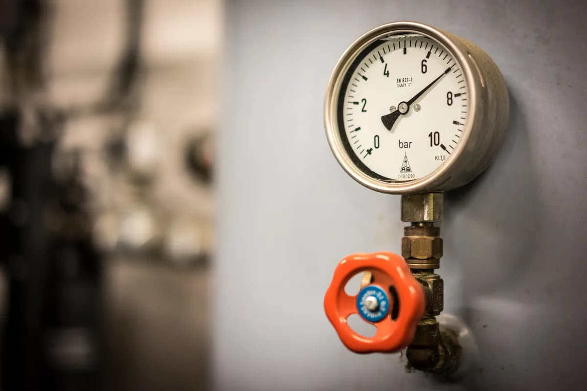 Industrial pressure gauge showing bar measurement with red valve handle on gas pipeline